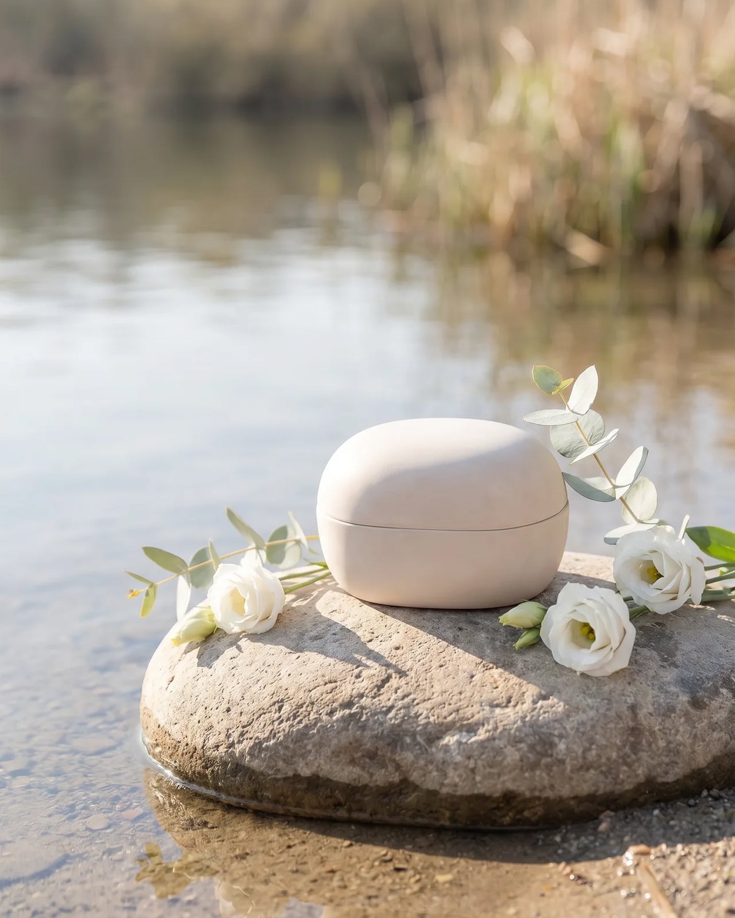 Biodegradable cremation urn for water burial — eco-friendly clay urn with white flowers by the river