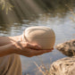 Eco-friendly cremation urn held in hands near water — natural clay biodegradable urn for water scattering